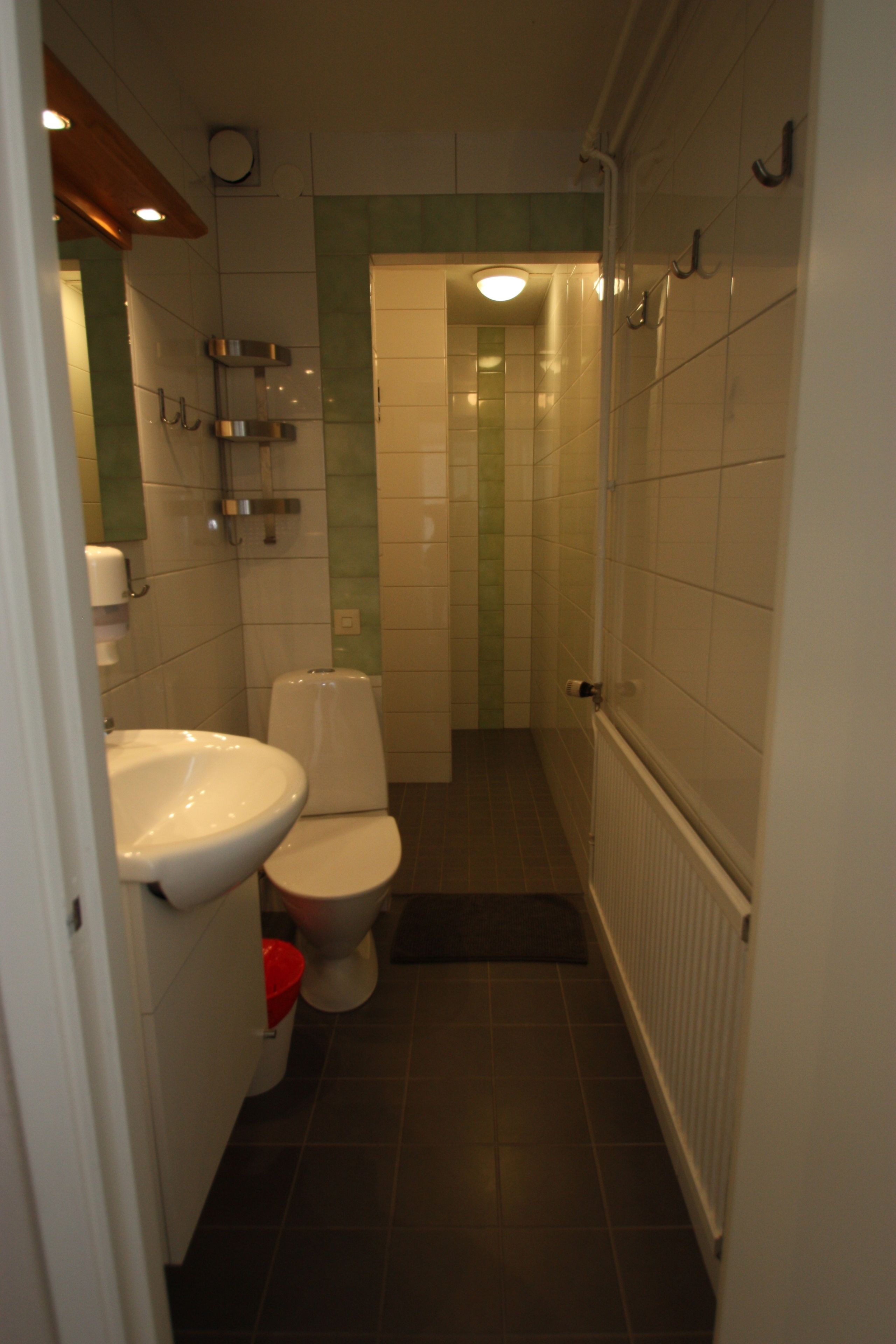 Un baño estrecho con lavamanos, inodoro y zona de ducha, todo en blanco.