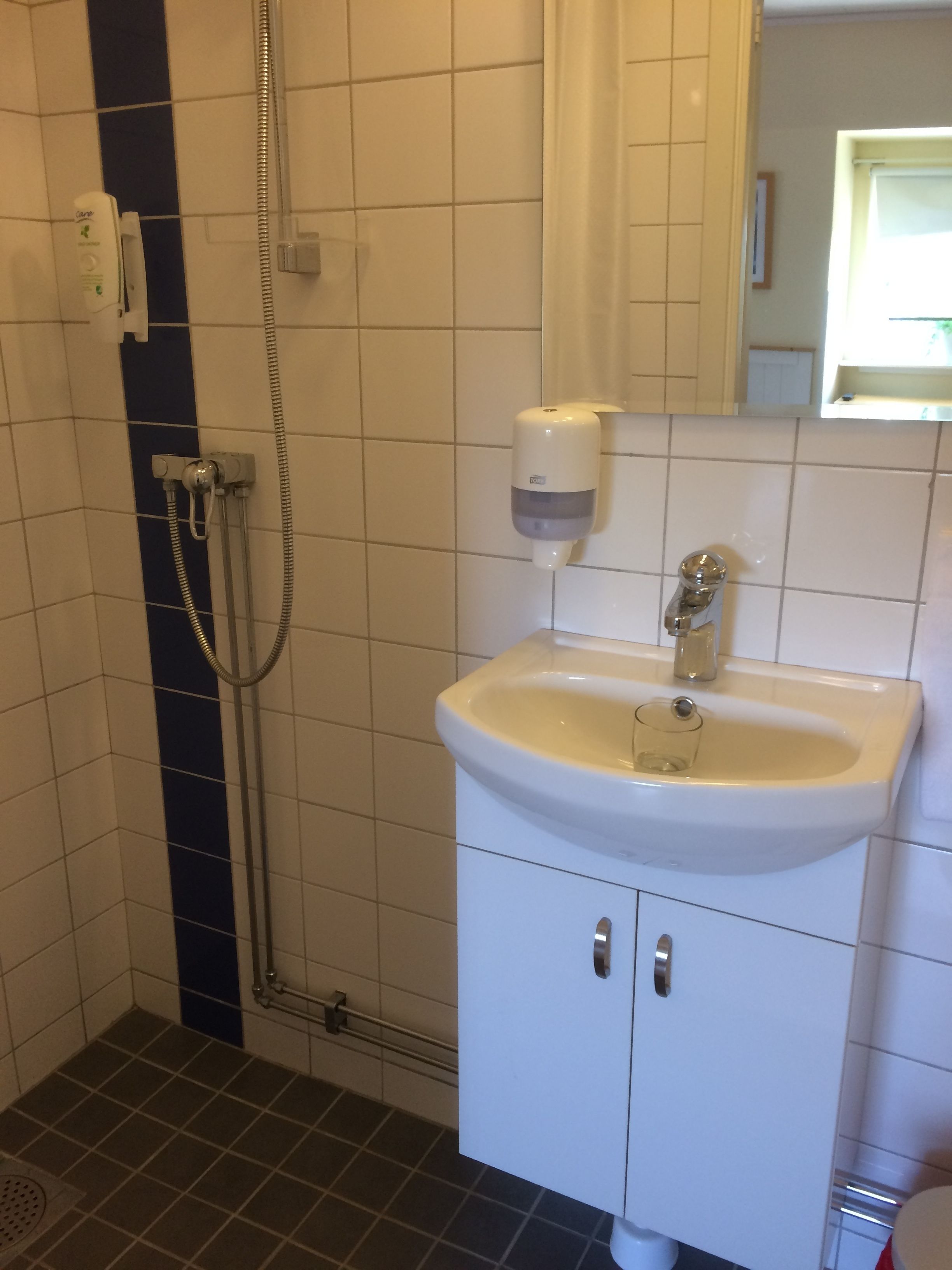 Un baño con un lavamanos blanco, un espejo y una ducha con cabezal de ducha de mano.