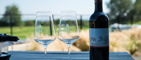 A bottle of wine and two glasses on a wooden table with a blurred outdoor background.