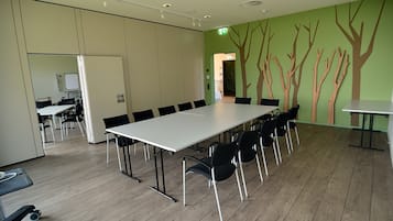 A conference room with a long table and chairs, a whiteboard, and a green wall with tree decorations.