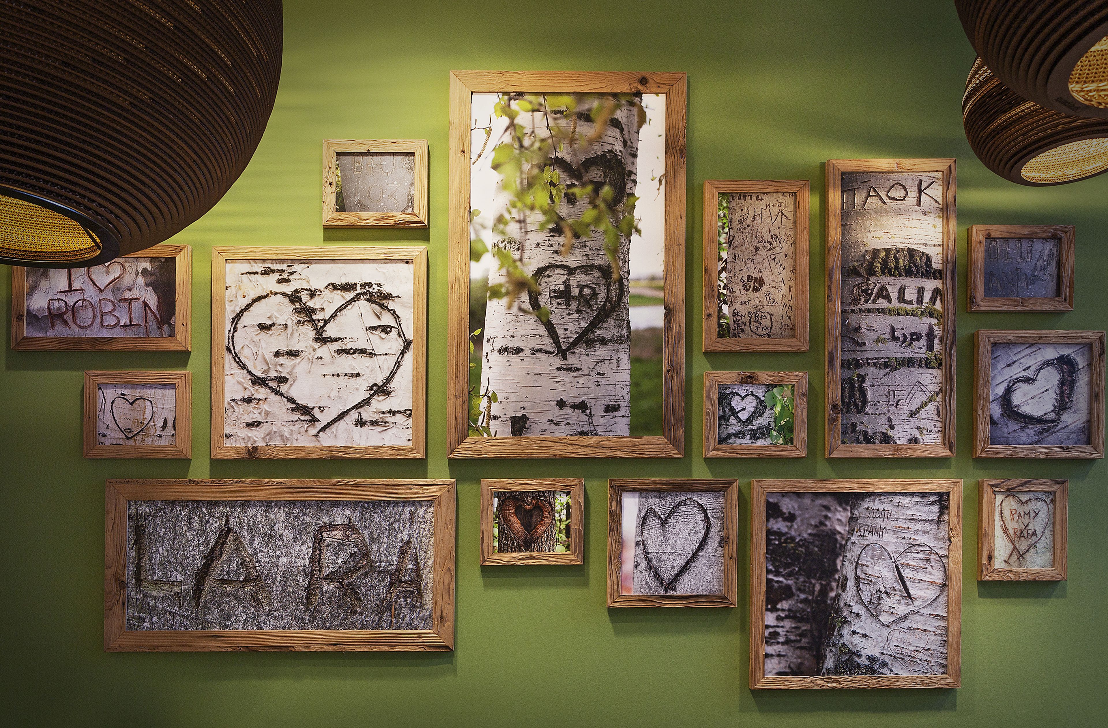 A wall with multiple framed artworks, including heart shapes and text, against a green background.