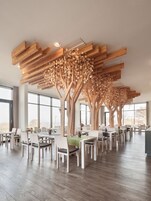 Ein großzügiger Essbereich mit Holzbalken an der Decke, die an Bäume erinnern, großen Fenstern und modernen Möbeln.