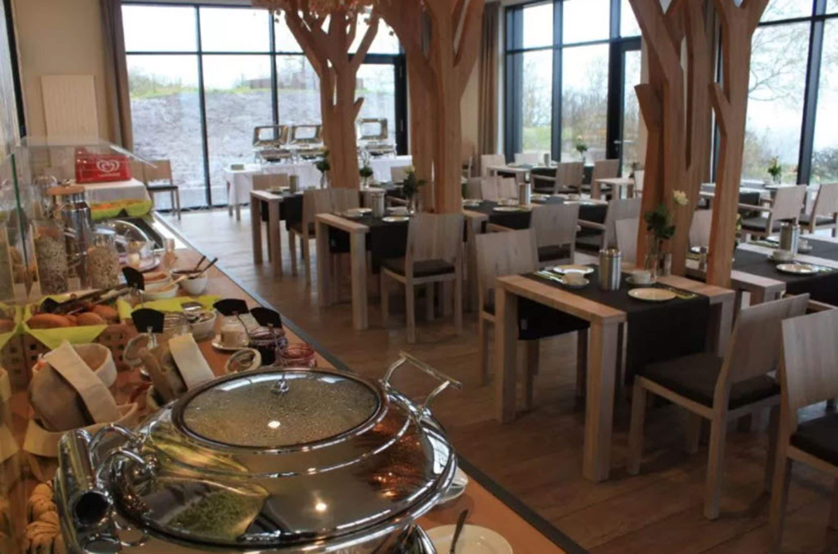 A restaurant with multiple dining tables and chairs, large windows, and a buffet area with various food items.