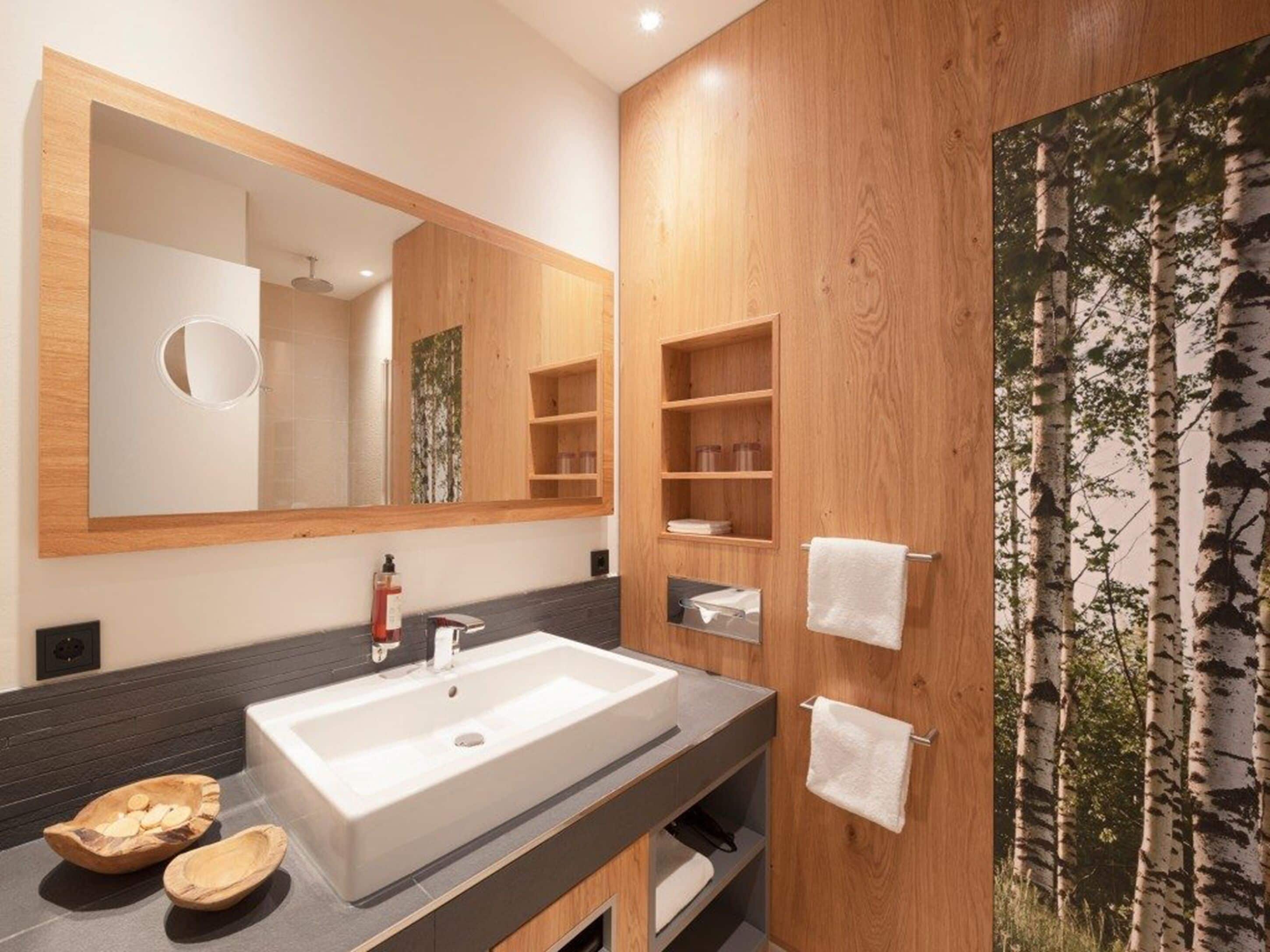 Ein modernes Badezimmer mit einem großen Spiegel, einem Holzkosmetikschrank und einem Waschbecken.