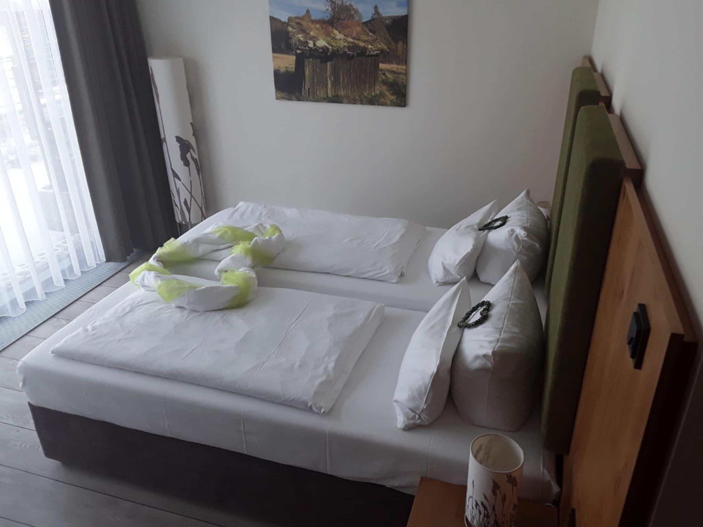 A neatly made bed with white linens and decorative pillows, a wooden headboard, a framed picture on the wall, and a window with sheer curtains.