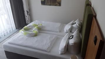 Een net opgemaakt bed met witte lakens en decoratieve kussens, een houten hoofdbord, een ingelijst beeld aan de muur en een raam met dunne gordijnen.