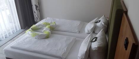 Una cama bien hecha con sábanas blancas y almohadones decorativos, un cabecero de madera, un cuadro en la pared y una ventana con cortinas de encaje.