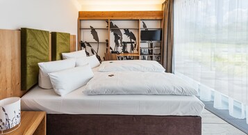 Ein modernes Schlafzimmer mit einem großen Bett, einem Holzkopfende, einem Fernseher und Blick ins Freie.