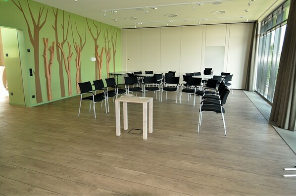 A conference room with a modern design, featuring a wooden floor, black chairs arranged in a semi-circle, and a central table.
