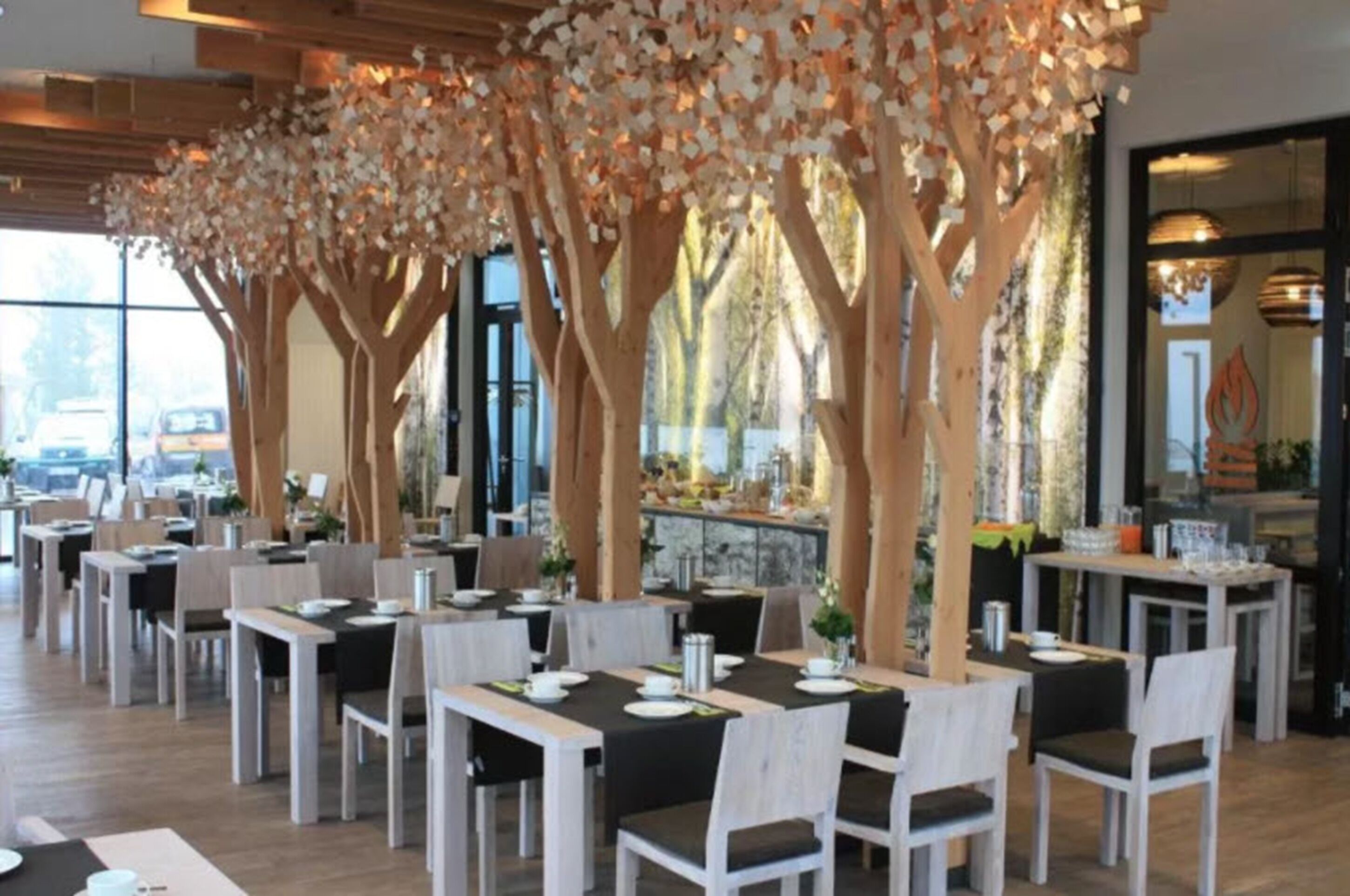 Un restaurante con varias mesas y sillas, techo de madera y ventanas amplias.