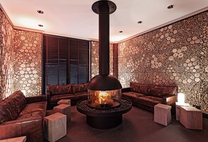 Eine moderne Lounge mit einem zentralen Kaminofen, Ledersofas und einem außergewöhnlichen Wanddesign.
