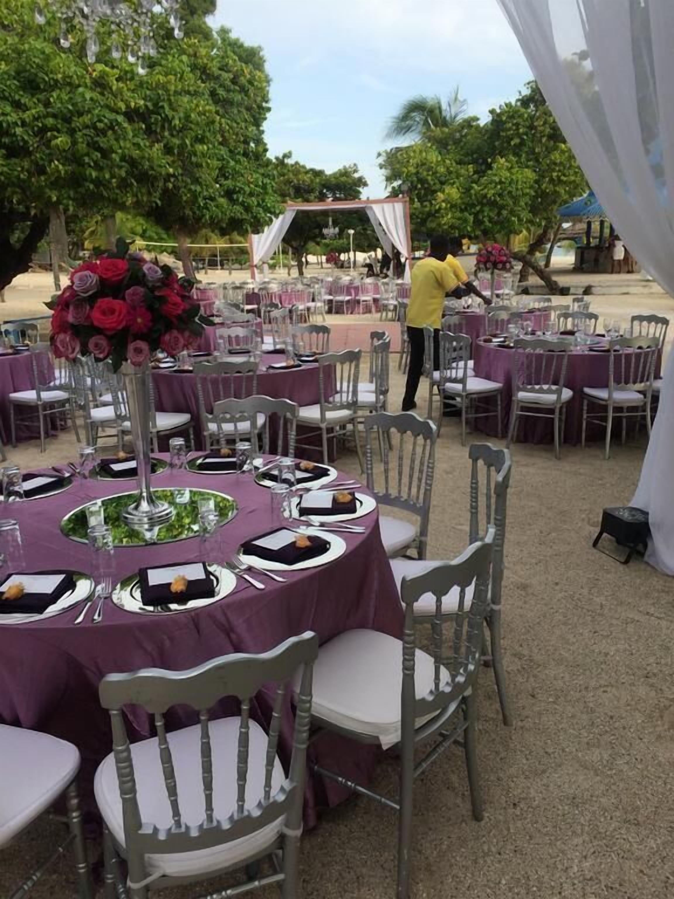 An outdoor event space with round tables covered in purple tablecloths, white chairs, and floral centerpieces.