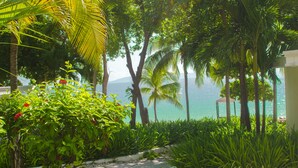 A tropical garden pathway leading to a beach with palm trees and lush greenery. - Kaliko Beach Club - All Inclusive Resort (Arcahaie)