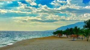 A beach with a clear sky, calm sea, and palm trees. - Kaliko Beach Club - All Inclusive Resort (Arcahaie)