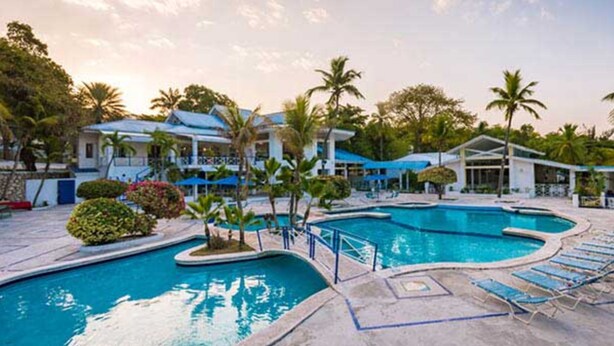 A resort with a large swimming pool, palm trees, and modern buildings. - Kaliko Beach Club - All Inclusive Resort (Arcahaie)
