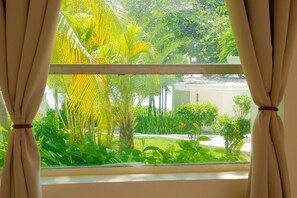 Ein Fenster mit Vorhängen, Blick auf einen üppigen Garten mit verschiedenen Pflanzen und Bäumen.