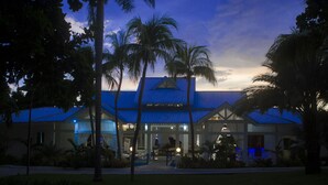 A hotel with a blue roof, palm trees, and a well-lit entrance. - Kaliko Beach Club - All Inclusive Resort (Arcahaie)