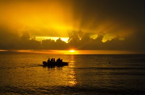 Ein Sonnenuntergang über dem Meer mit einem Boot, das Menschen transportiert.