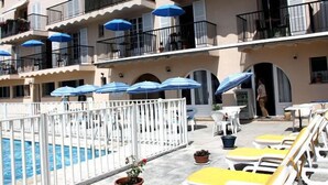 A hotel with a pool area, outdoor seating, and multiple balconies with blue umbrellas. - Hôtel de la Poste (Peymeinade)