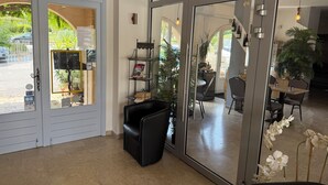 A modern interior with a glass door entrance, a seating area with black chairs, and a dining space with a table and chairs. - Hôtel de la Poste (Peymeinade)