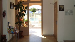 A hallway leading to a pool area with a potted plant and a small table with magazines. - Hôtel de la Poste (Peymeinade)