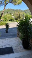 Una entrada pavimentada con plantas en macetas, una vista despejada de un paisaje montañoso y un edificio distante.