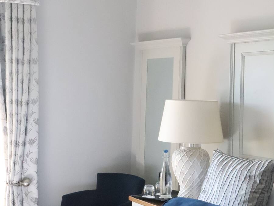 Ein Hotelzimmer mit Bett, Schreibtisch, Stuhl, Lampe und einem Fenster mit Vorhängen.