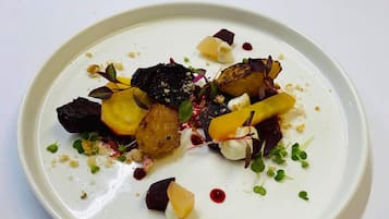 A white plate with a variety of food items including what appears to be roasted potatoes, beetroot, and possibly some greens, arranged on a white tablecloth.
