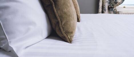 A bed with white bedding and two pillows, one white and one brown.