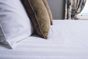 A bed with white bedding and two pillows, one white and one brown. - Causeway Hotel (Bushmills)