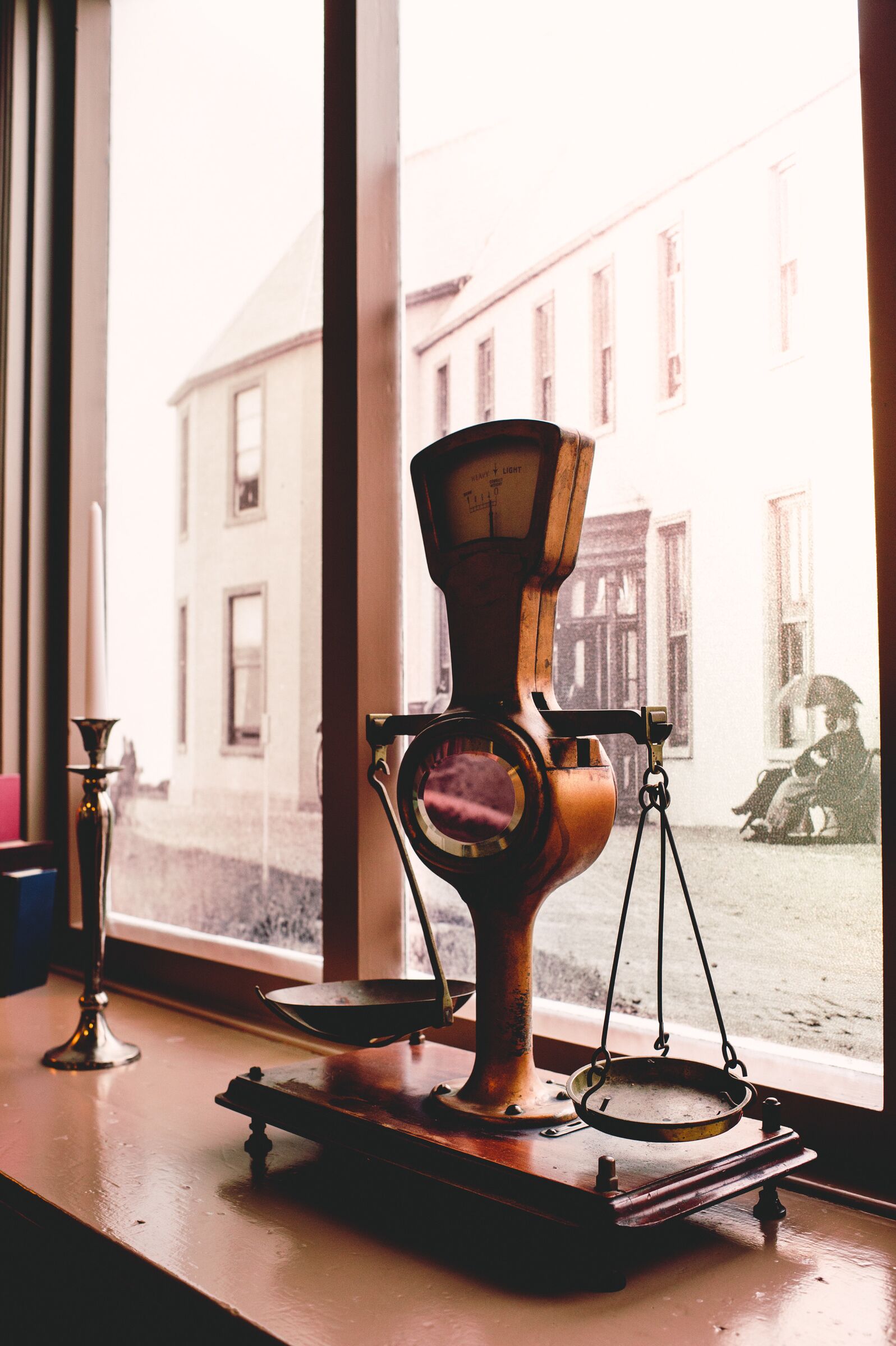 A vintage scale on a windowsill with a view of buildings outside.
