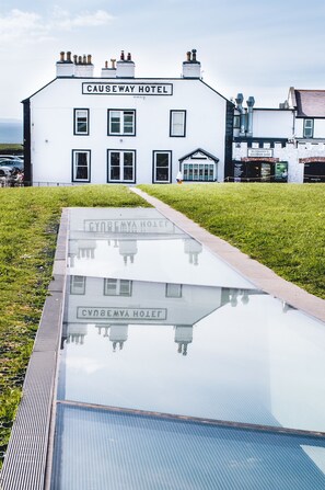 A white building with a sign reading "Causeway Hotel" and a reflection on its glass surface. - Causeway Hotel (Bushmills)