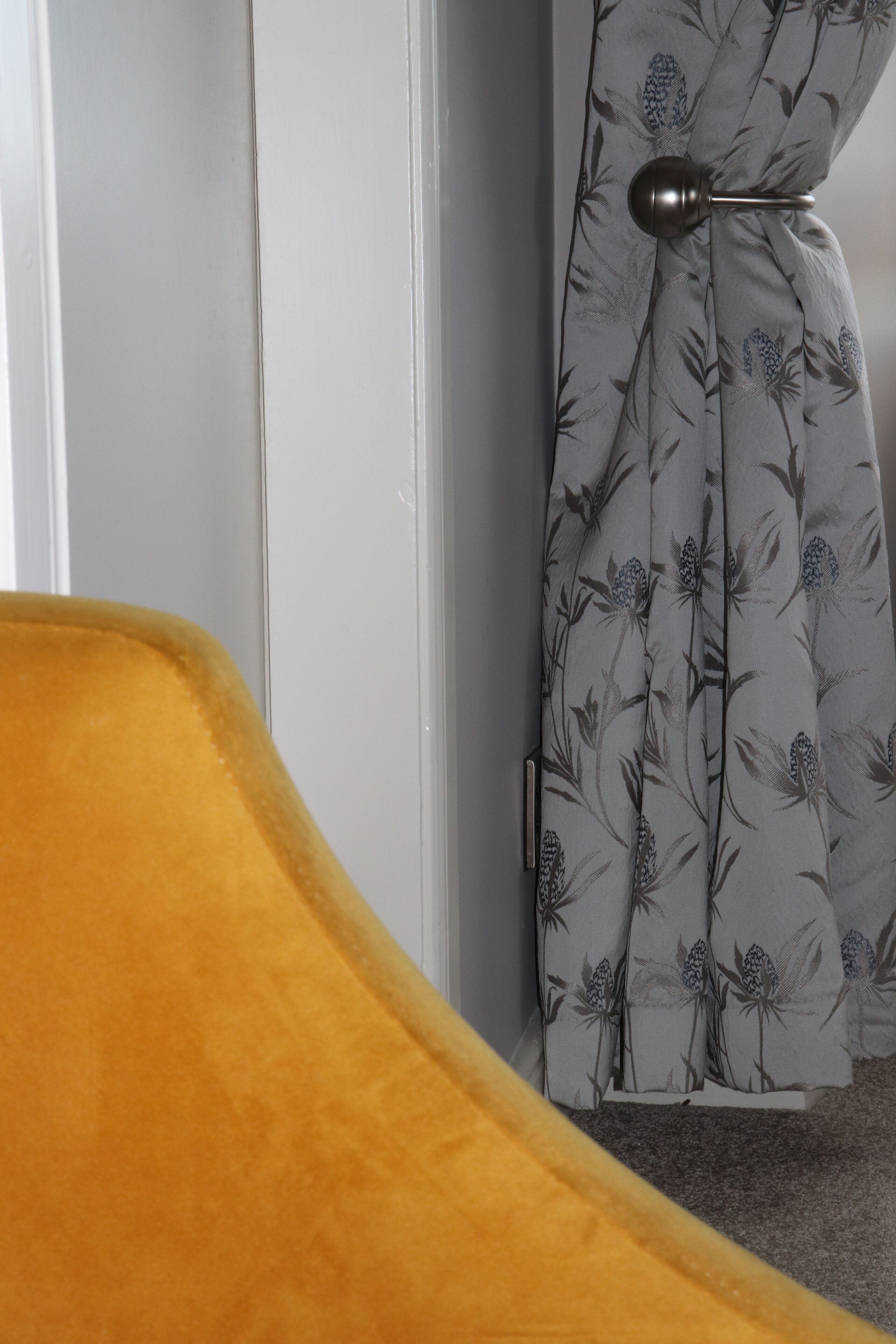 A room with a yellow armchair, a white door, and a curtain with a floral pattern.