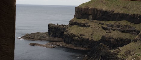 A coastal view from a stone structure with a wooden railing, overlooking a rocky shoreline and the sea.