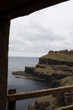 A coastal view from a stone structure with a wooden railing, overlooking a rocky shoreline and the sea. - Causeway Hotel (Bushmills)