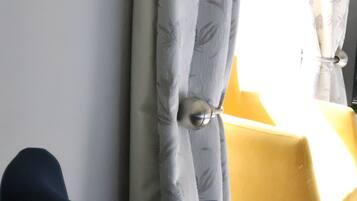 Una habitación con una silla de color oscuro, una mesa amarilla y cortinas claras con un estampado floral.