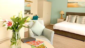A hotel room with a bed, a chair, a table with a book and a vase of flowers.