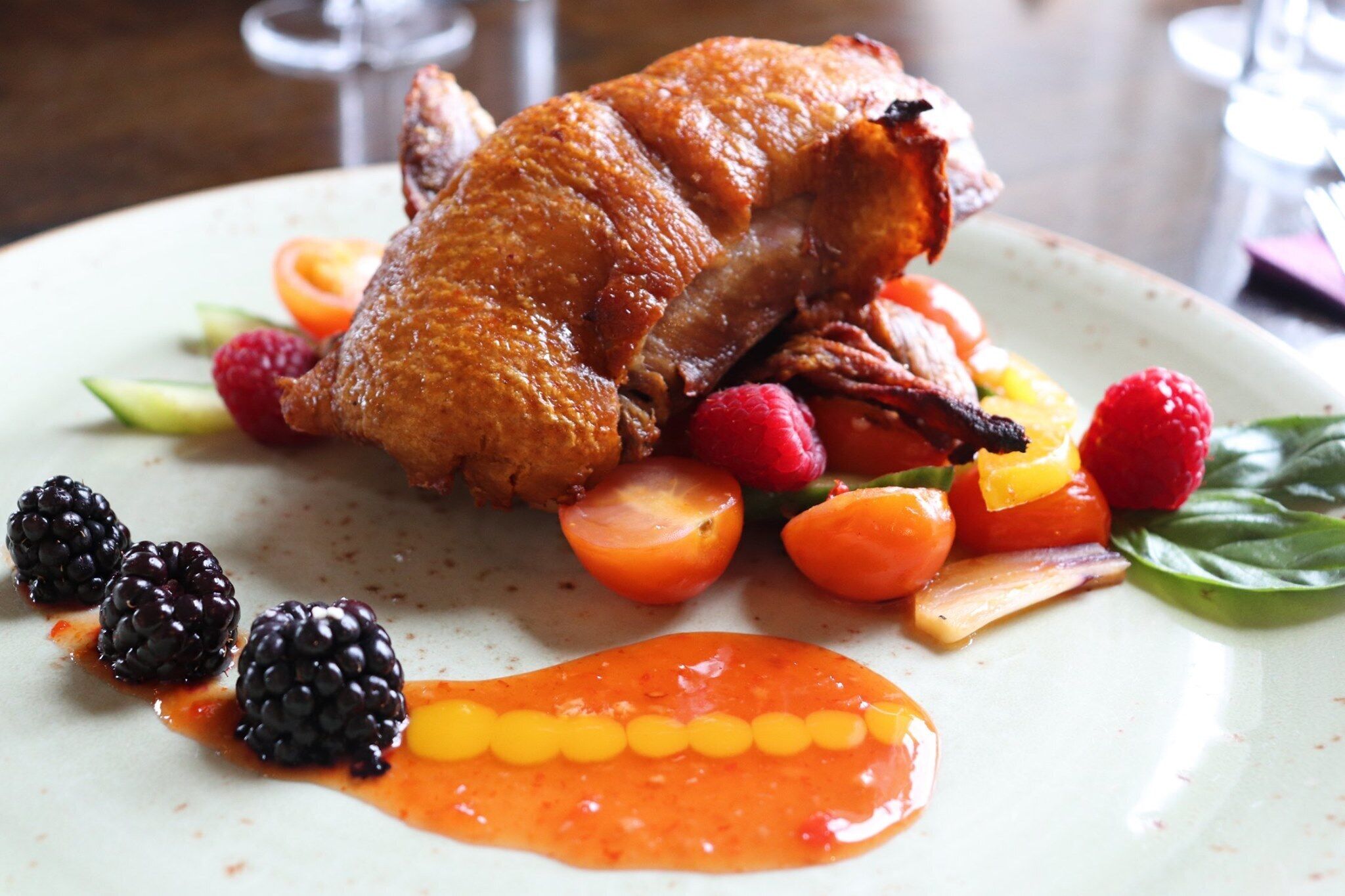 A roasted duck served with vegetables and berries on a plate.