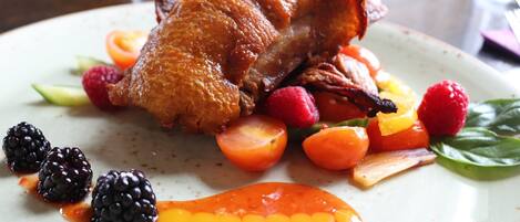 A roasted duck served with vegetables and berries on a plate.