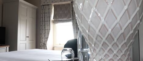 A hotel room with a bed, a bedside table with glasses and a cup, a wardrobe, and a window with curtains.