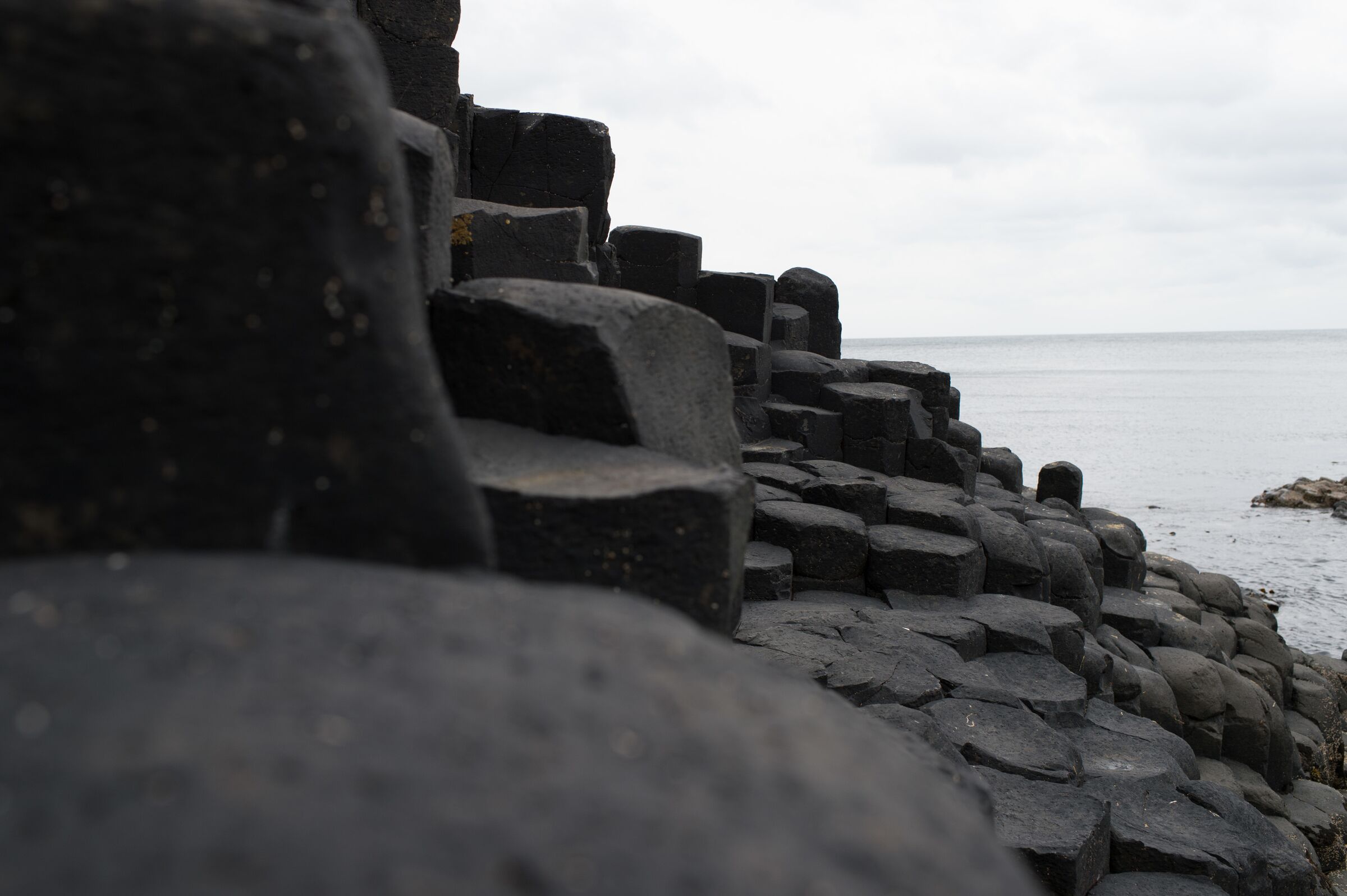 A stone wall with a rough texture, leading to a body of water.