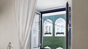 Una habitación con una silla blanca, una ventana con contraventanas azules y un radiador blanco.