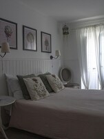 Un dormitorio con una cama grande, dos lámparas fijadas a la pared y tres impresiones enmarcadas de motivos botánicos.