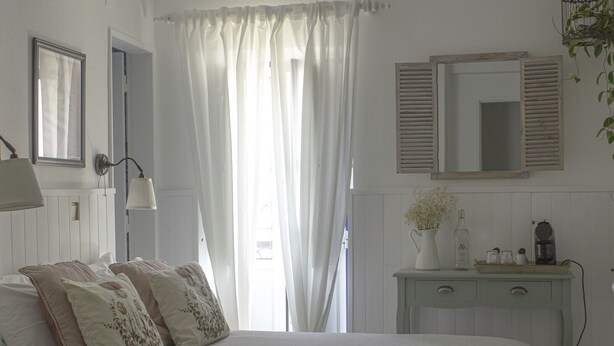 Un dormitorio con cama, mesita de noche, cómoda, espejo y ventana con cortinas.