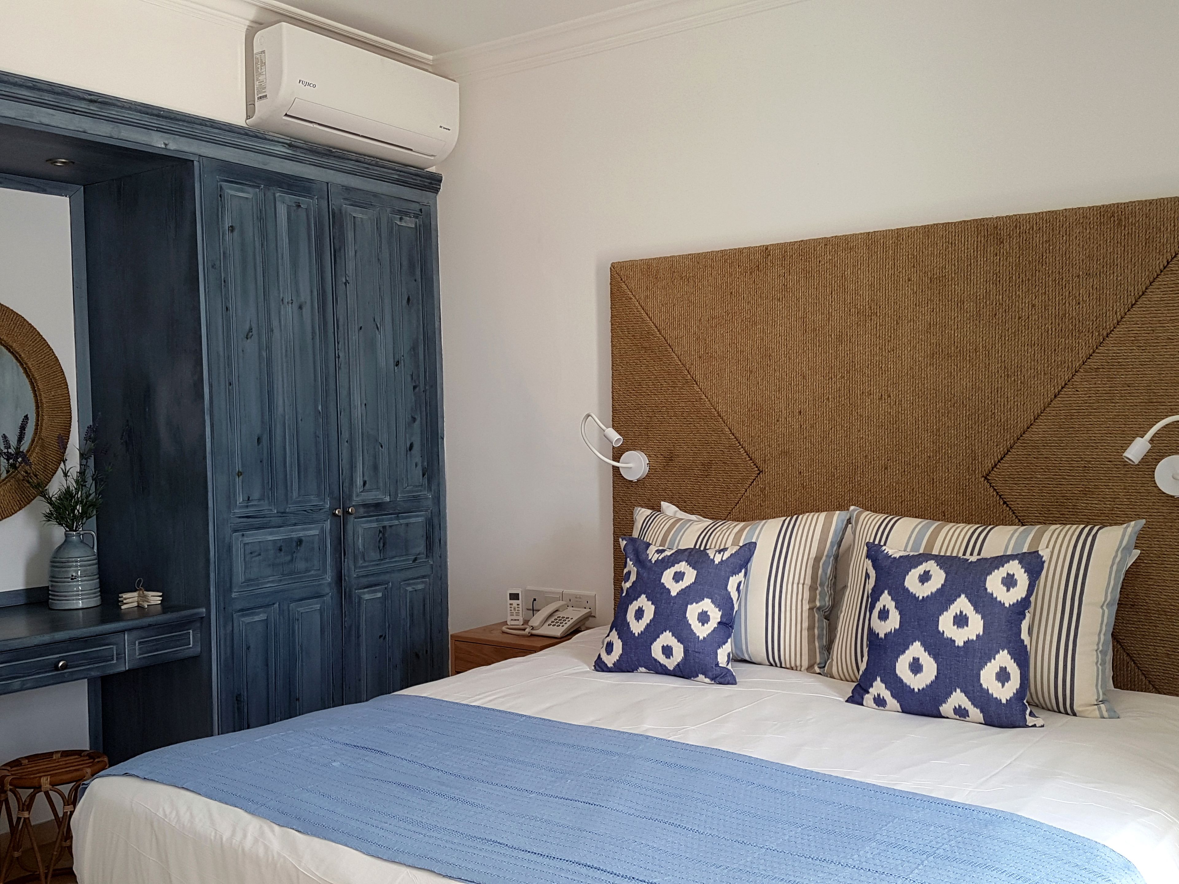 Un dormitorio con una cama grande, un armario, una mesita de noche con lámpara y aire acondicionado instalado en la pared.