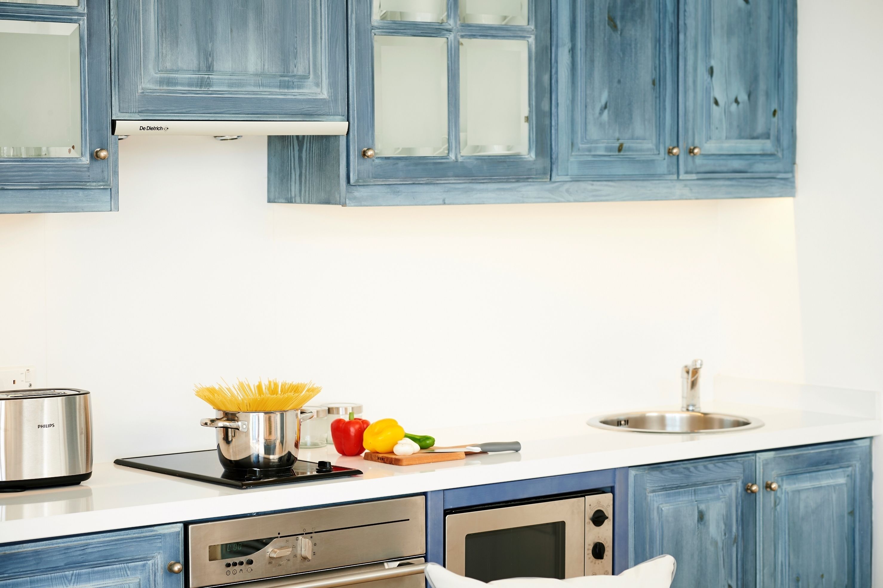 A modern kitchen with blue cabinets, a stainless steel sink, a built-in oven, and a digital clock.