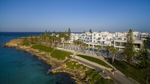 A coastal hotel with a pool, multiple balconies, and a view of the sea. - Nausicaa Luxury Villas By Louis Hotels (Paralimni)
