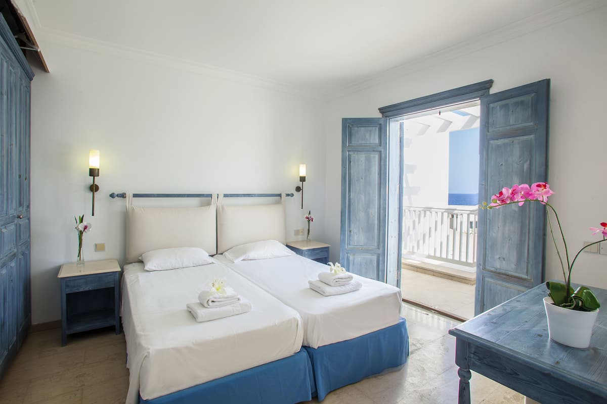 Een hotelkamer met twee bedden, een balkon met uitzicht en een potplant.
