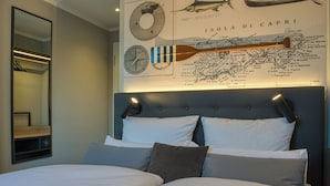 A hotel room with a large bed, a headboard with lights, a map of Capri on the wall, and a mirror on the left. - UNO Hotel Hamburg Central 053 (Hamburg)