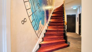 A staircase with red carpet, a wall with abstract art, and a door in the background. - UNO Hotel Hamburg Central 053 (Hamburg)